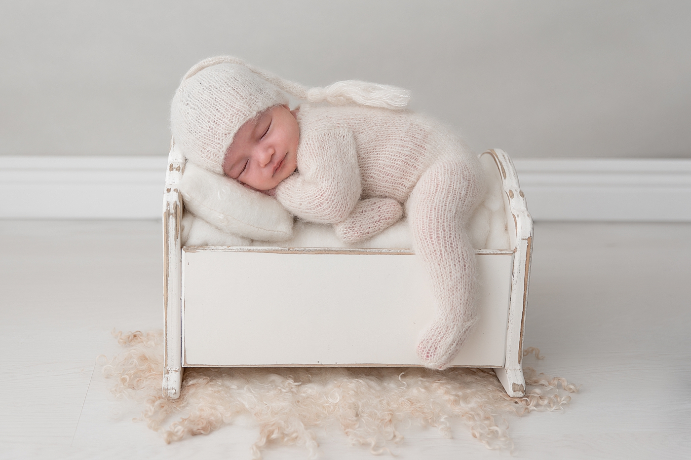 Posed newborn photo of baby boy sleeping on a small bed. Photo by Rachel Brookes Photography.