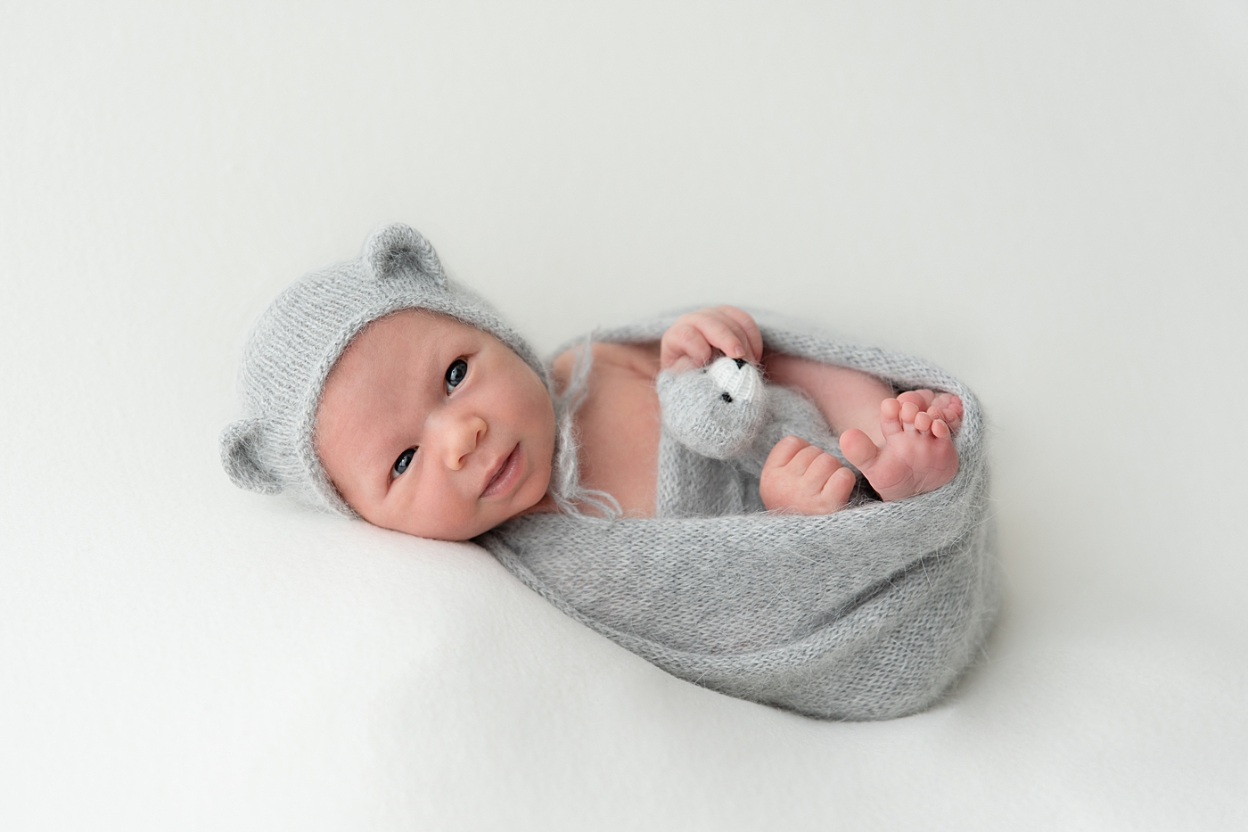 Baby boy in grey knit swaddle and hat for newborn photos. Photo by Rachel Brookes Photography.