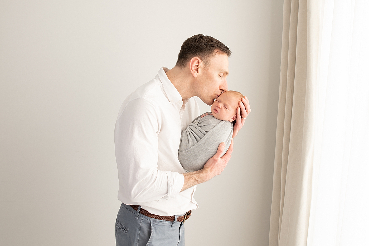 Dad giving his son a kiss during newborn photoshoot. Photo by Rachel Brookes Photography.