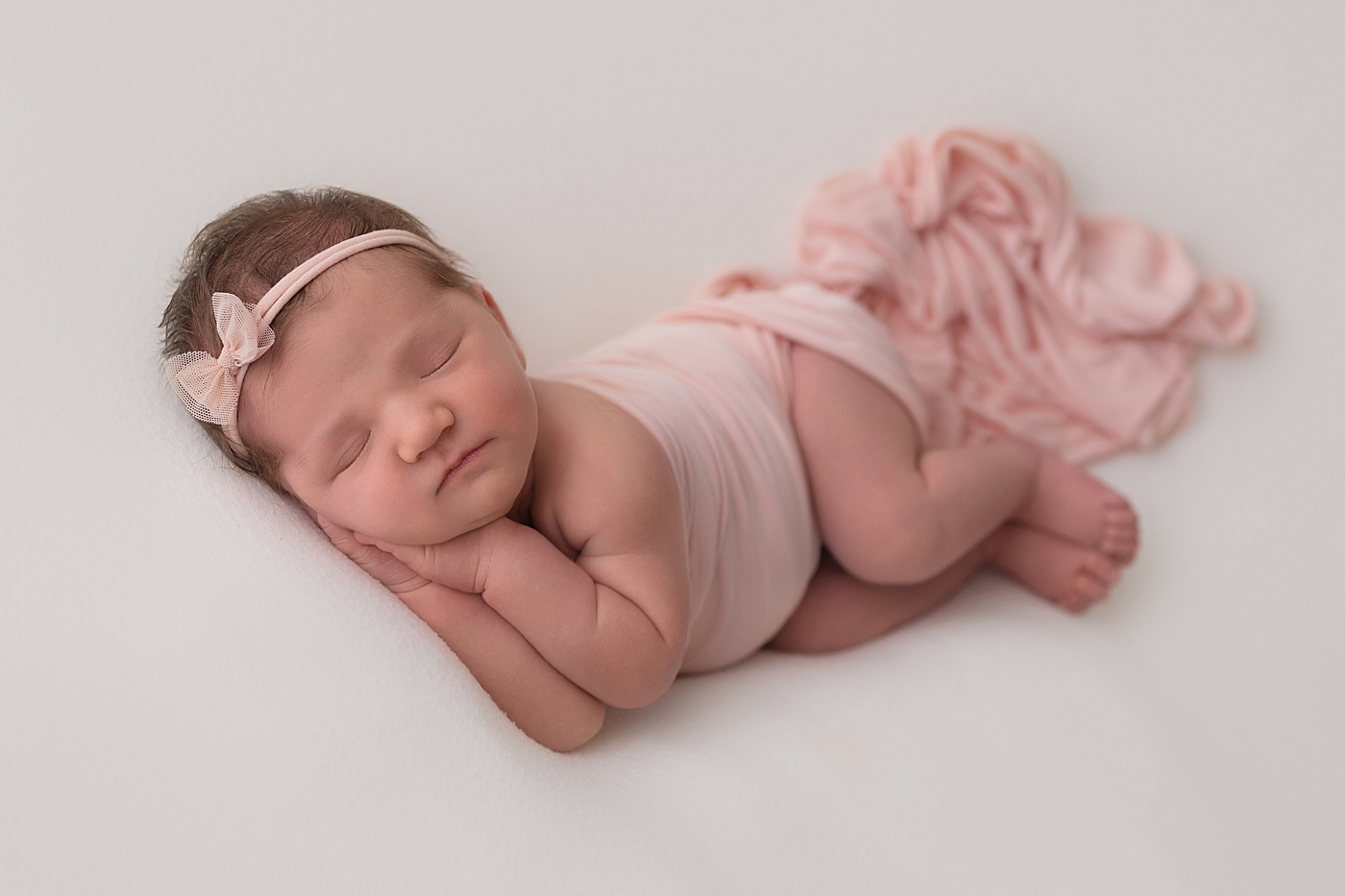 Baby girl posed on her side wearing pink for newborn photos. Photo by Rachel Brookes Photography.
